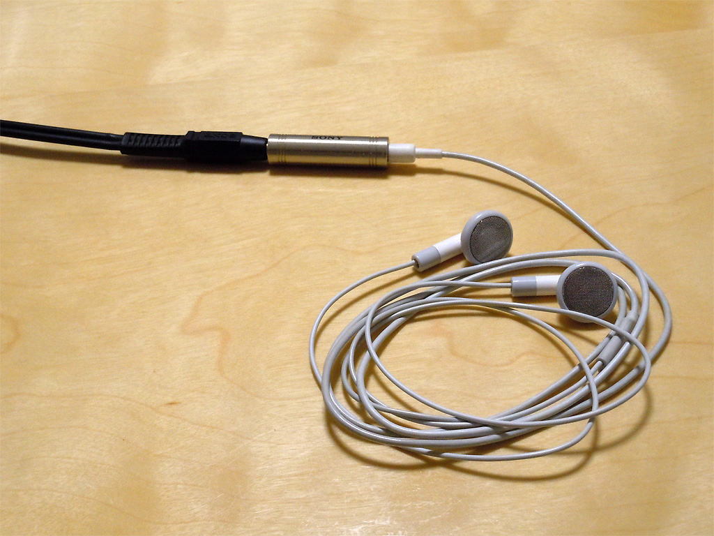 SONYの3.5mm オーディオコードとiPod付属イヤホンを中継コネクタで繋いだ物が食卓の上を這っている写真 SONYの3.5mm オーディオコードとiPod付属イヤホンを中継コネクタで繋いだ物が食卓の上を這っている写真