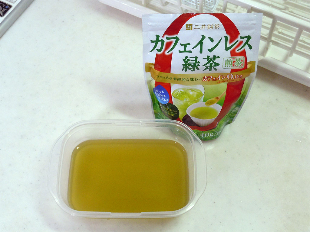 白い調理台に置かれたカフェインレス緑茶のチャック袋とタッパーに作った緑茶ゼリーの写真