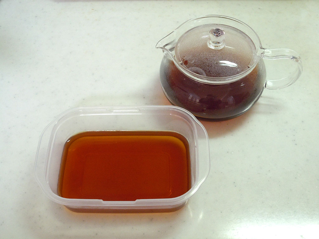 白い調理台に置かれたガラスポットに入ったルイボスティーとタッパーに作ったルイボスティーゼリーの写真 